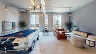 Located at 107 Wardlaw St in Greenville, South Carolina, this single-floor lobby and amenity space presents a striking blend of industrial and contemporary design. The expansive open-plan layout is anchored by polished light-toned tile flooring and soaring ceilings with exposed ductwork, steel-framed columns, and striking circular acoustic panels that contribute to both the aesthetic and acoustic quality of the space.

The main lounge area is bathed in abundant natural light streaming through floor-to-ceiling windows, offering views of the surrounding Greenville streetscape. Curated seating arrangements — featuring leather sofas, velvet accent chairs in deep blue with gold frames, and a vivid teal watercolor-inspired area rug — create an inviting and artful atmosphere. Statement pendants with Edison-style bulbs and a dramatic large-scale painting add to the gallery-like character of the space.

Integrated throughout the lobby are lush planters and potted tropical greenery, bringing warmth and a biophilic quality to the industrial setting. A dedicated mail room, finished with warm gray textured walls, gold trim accents, a globe chandelier, and framed artwork, provides a refined and functional amenity. A slatted wood accent wall with moss art installations further enhances the lobby's distinctive, design-forward identity.