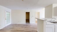 Located at 8930 Mont Carmel Ln in Charlotte, NC, this single-floor, 2-bedroom, 3-bathroom home offers a practical and well-organized layout. The open-concept living area features light wood-look flooring that extends throughout the main living spaces, creating a clean and cohesive aesthetic. A peninsula with granite-style countertops connects the kitchen to the living room, providing both functional workspace and a casual dining option. The galley-style kitchen is equipped with white cabinetry, a stainless steel sink, and white appliances including a range and refrigerator, all bathed in natural light from a nearby window. The living area includes a glass-paneled entry door and a side window, bringing in additional natural light and a view of surrounding greenery. Both bedrooms are carpeted for comfort, with the primary bedroom offering a dedicated walk-in closet featuring built-in wire shelving. The bathrooms are finished in a clean, neutral palette, with at least one full bath featuring a tub-shower combination and a single vanity. A dedicated exercise room adds functional versatility to the floor plan. Textured ceilings and white trim throughout complete the tidy, neutral interior of this Charlotte home.