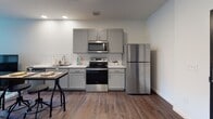 Located at 9600 Hough Ave in Cleveland, OH, this thoughtfully designed single-floor unit offers a modern, open-concept layout with rich hardwood-style flooring and a clean, neutral color palette throughout. The kitchen is well-appointed with gray shaker-style cabinetry, white subway tile backsplash, white countertops, and a full suite of stainless steel appliances including a refrigerator, electric range, and over-the-range microwave. A dining area sits adjacent to the kitchen, making everyday meal prep and entertaining convenient. The living area features large windows that invite natural light and offer outdoor views, creating a bright and welcoming atmosphere. The bedroom is a quiet, comfortable retreat with ample space and direct access to a walk-in closet with built-in shelving for generous storage. The bathroom is finished in crisp white tones, featuring a walk-in glass-door shower with tiled walls, a white vanity with an integrated sink, and hardwood-style flooring that ties seamlessly to the rest of the unit. The overall design balances modern finishes with functional living, making this a well-rounded and practical space in the heart of Cleveland's Hough neighborhood.