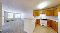 Located at 5000 Lydianna Ln in Suitland, MD, this one-bedroom, one-bathroom apartment offers a practical and comfortable single-floor layout. The open-concept design connects the kitchen and living room seamlessly, creating a functional shared living space. The kitchen features warm honey-toned oak cabinetry, light countertops, tile flooring, and a full suite of white appliances including a refrigerator, electric range, dishwasher, and under-cabinet ventilation hood. A peninsula counter separates the kitchen from the carpeted living area, providing a convenient breakfast bar or prep space. The living room receives natural light through a large window and is finished with plush, neutral-toned carpet that extends throughout the main living areas. The bedroom is a well-proportioned retreat with two large windows fitted with blinds, allowing for natural light and outdoor views of the surrounding neighborhood. A wall-mounted HVAC unit provides individual climate control. The bathroom includes a vanity with wood cabinetry, a wall mirror, a tub-shower combination, and tile flooring. Two closets offer convenient storage throughout the unit. Overall, the space maintains a clean, neutral aesthetic well-suited for comfortable everyday living.