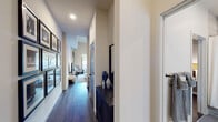 This single-floor residence showcases a contemporary design with a cohesive blend of modern finishes and warm, inviting tones. Dark hardwood flooring flows throughout, anchoring each room with a sense of continuity and sophistication.

The entry hallway sets an elegant tone, featuring a gallery-style wall arrangement of framed artwork and a navy blue accent console with decorative ceramic vases. It leads seamlessly into the main living area, where a comfortable, light-filled space centers around a leather sofa, sleek media console, and a large sliding glass door that opens to a private outdoor balcony with natural views.

The kitchen is efficiently laid out with white quartz countertops, a marble-style tile backsplash, dark cabinetry, a black cooktop, and a bold range hood. Under-cabinet lighting and a bright window overlooking the balcony enhance the functional yet stylish workspace.

The primary bedroom offers elevated ceilings and a tranquil atmosphere, complete with open shelving and direct access to an en-suite bathroom. The bathroom features large-format tile surrounding a soaking tub and shower combination, a wood-toned vanity, matte black fixtures, and tile flooring.

A second bedroom provides a cozy, well-appointed retreat with soft neutral walls and room for a full bed. Throughout, recessed lighting and clean architectural lines contribute to the polished, modern ambiance of this well-designed residence.