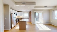 Located at 1810 Airport Rd in Colorado Springs, CO, this single-floor unit offers a clean, modern aesthetic throughout. The open-concept kitchen is a standout feature, designed with a dual-tone cabinetry scheme pairing sleek white upper cabinets with warm wood-toned lower cabinets. Stainless steel appliances — including a refrigerator, range, microwave, and dishwasher — complement the light quartz countertops and a central kitchen island, providing both additional workspace and visual definition within the layout. Light hardwood flooring flows consistently throughout the space, lending warmth and continuity. Recessed lighting and large windows allow natural light to fill the interior, with sunlight casting bright patterns across the floors. A sliding glass door opens directly onto an outdoor balcony, offering views of the surrounding Colorado landscape, including glimpses of the mountains. The bedroom is bright and simply finished, featuring vertical blinds that filter natural light, neutral walls, and the same hardwood flooring. The bathroom is functional and clean, outfitted with a full tub-shower combination, brushed nickel fixtures, and a classic white finish. The overall ambiance is contemporary, light, and move-in ready, with a consistent design language maintained across all rooms.
