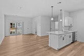 This newly constructed single-floor unit offers a clean, contemporary design throughout. The open-concept layout connects a spacious living area to the kitchen, both finished with light hardwood flooring that enhances the bright, airy atmosphere. The kitchen is well-appointed with white shaker-style cabinetry featuring black hardware, white countertops, a stainless steel sink, and a full suite of stainless steel appliances including a refrigerator and dishwasher. Pendant globe lighting fixtures hang above the kitchen island, adding a modern touch. The living area is generously sized with neutral white walls and ample room for flexible furniture arrangements, with sliding glass door access to an outdoor area. The bedrooms are carpeted for comfort and feature natural light from single-hung windows, along with double-door closets with black hardware. The bathroom is finished with wood-look flooring and includes a full tub-shower combo and toilet. A dedicated in-unit laundry room houses a full-size washer and dryer with overhead wire shelving for added storage. Throughout the unit, clean white walls, consistent trim work, and an electrical panel conveniently located near the entry complete this thoughtfully designed space.