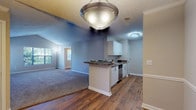 Located at 100 Preston Woods Trail in Sandy Springs, this single-floor residence features a thoughtfully designed open-concept layout that connects the living, dining, and kitchen areas seamlessly. The living area is finished with neutral-toned carpet and benefits from vaulted ceilings that enhance the sense of openness, while windows with blinds admit natural light and offer views of surrounding greenery.

The kitchen is configured in a galley style, featuring white shaker cabinetry on both sides, dark granite-style countertops, hardwood-style flooring, and stainless steel appliances including a refrigerator, range, microwave, and dishwasher. A peninsula with a pendant light separates the kitchen from the dining area, which is finished with matching hardwood-style flooring.

The bedrooms are carpeted and generously sized, each receiving natural light through sizable windows. The bathrooms include white vanity cabinetry, granite-style countertops, hardwood-style flooring, and well-lit vanity mirrors. A dedicated laundry room accommodates a full-size washer and dryer with overhead shelving. Neutral wall tones and textured ceilings are consistent throughout, contributing to a clean and cohesive aesthetic.