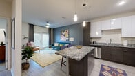 Located at 5110 S Manhattan Ave in Tampa, Florida, this single-floor residence showcases a thoughtfully designed open-concept layout with modern finishes throughout. Light wood-style flooring flows seamlessly through the main living areas, creating a bright and cohesive aesthetic.

The kitchen is a standout feature, boasting granite countertops, a large center island with bar seating, two-tone cabinetry — crisp white uppers paired with dark wood lowers — a subway tile backsplash, and a full suite of stainless steel appliances. Pendant lighting adds a refined touch overhead.

The open living area is generous and welcoming, with large sliding glass doors that invite natural light and provide outdoor access. A ceiling fan, dedicated workspace with a granite-topped built-in desk, and a smooth transition from dining to lounge areas make the layout both functional and comfortable.

The bedrooms feature plush carpeting, large windows with draping curtains, and ample space for rest and storage. The bathroom is well-finished with granite vanity countertops, dark wood cabinetry, a tub-shower combination, and light tile flooring that continues the home's clean, contemporary theme throughout.