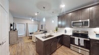 This well-appointed single-floor residence offers a thoughtfully designed open-concept layout that seamlessly connects the kitchen and living areas. The kitchen is a standout feature, showcasing rich dark espresso cabinetry, crisp white quartz countertops, a classic subway tile backsplash, and a full suite of stainless steel appliances including a range, microwave, dishwasher, and a French door refrigerator. A peninsula with an undermount sink and elegant pendant lighting serves as both a functional workspace and a natural gathering point, while also providing a smooth visual transition into the living area. Warm wood-look flooring flows consistently throughout the entire residence, adding cohesion and a sense of warmth to every room. The living area is bright and comfortable, featuring a ceiling fan, a large window with blinds, and direct access to a private exterior door, allowing for natural light and easy outdoor access. Both bedrooms are well-proportioned, each featuring ceiling fans, ample natural light from large windows with blinds, and the same warm flooring found throughout the home. The overall aesthetic is modern and clean, with a neutral color palette of soft whites and warm grays that creates a calm, inviting ambiance throughout the space.