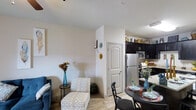 Located in White Settlement, this single-floor residence offers a thoughtfully designed open-concept layout that seamlessly connects the living, dining, and kitchen areas into one cohesive space. The living area provides a comfortable retreat, accented by light-toned walls and wood-look flooring that extends throughout the unit, lending a warm and inviting atmosphere. A cozy accent chair and small side table anchor the sitting area, while decorative wall accents add a personalized touch.

The dining space flows naturally from the living area and features a compact round dining table with black chairs, ideal for intimate meals. Adjacent to the dining area, the kitchen is well-appointed with dark espresso cabinetry, stainless steel appliances including a full-size refrigerator and microwave, and light countertops that provide a striking contrast against the dark cabinets. Upper shelving above the cabinets offers additional display and storage space.

A paneled interior door provides access to additional areas of the home, maintaining a clean and classic architectural detail. The overall ambiance is bright and airy, with neutral wall tones and consistent flooring creating a unified, modern aesthetic throughout this efficiently designed single-story residence.