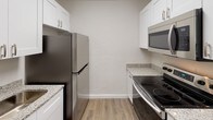 This single-floor unit offers a clean, contemporary layout designed for functional everyday living. The kitchen is well-appointed with white shaker-style cabinetry, granite-look countertops, and a full suite of stainless steel appliances, including a refrigerator, electric range, and over-the-range microwave. Durable wood-look vinyl flooring runs throughout, providing a cohesive and easy-to-maintain finish across the space. The open living area is bright and spacious, with neutral white walls and a seamless sightline into the kitchen and laundry area, where an in-unit washer is conveniently tucked beneath the cabinetry. Two well-proportioned bedrooms each feature their own closet storage — one with a reach-in closet with a hanging rod, and the other with a double-door sliding closet — both rooms continuing the dark-toned vinyl flooring for a grounded, modern feel. The bathroom is finished with large-format gray stone-look wall tile surrounding a soaking tub and shower combo, complemented by brushed nickel fixtures and granite-accented vanity details. The overall aesthetic is fresh, neutral, and move-in ready, with consistent finishes that lend the space a cohesive and updated character throughout.