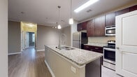 Located at 9005 Post Canyon Ln in Charlotte, NC, this single-floor residence offers a well-appointed layout with modern finishes throughout. The kitchen serves as a central highlight, featuring a large granite-topped island with an undermount sink and a sleek pull-down faucet, complemented by rich dark cabinetry and a full suite of stainless steel appliances including a refrigerator, range, and built-in microwave. Pendant lighting above the island adds a polished touch, while light wood-style flooring flows through the main living areas. The open living and dining area is finished with crown molding and a ceiling fan, creating a bright and comfortable gathering space. The bedrooms are carpeted for warmth and comfort, each featuring ceiling fans and generous windows fitted with blinds that allow ample natural light and views of the surrounding landscape. Closet space is well provided, with sliding-door closets offering built-in shelving and hanging rods. The bathrooms are finished with granite-topped dark vanities and full tub-shower combinations with light wood-style flooring. A dedicated in-unit laundry room with overhead shelving adds everyday convenience, completing this thoughtfully designed residence.
