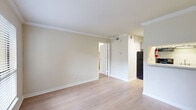 Located at 2400 Briarwest Blvd in Houston, TX, this one-bedroom, one-bathroom unit offers a well-organized and efficient single-floor layout. The combined kitchen and living area forms the heart of the space, featuring light wood flooring and crown molding throughout. The kitchen is equipped with a pass-through granite-style countertop bar, white cabinetry, a sink, and full-size appliances including a refrigerator and range, making it functional and accessible from the living area. The living room benefits from a large window that invites natural light and provides outdoor views of the surrounding greenery, creating a bright and welcoming atmosphere. Crown molding along the ceilings adds a classic architectural touch throughout the common areas. The generously sized primary bedroom is carpeted for comfort and features a ceiling fan, a window with outdoor views, and crown molding consistent with the rest of the unit. A dedicated closet provides convenient storage. The bathroom is clean and straightforward, featuring a combined shower and bathtub with tiled surrounds and wood-look flooring. The overall color palette is neutral and warm, with soft beige tones on the walls complementing the light flooring, lending the space a calm and cohesive ambiance.