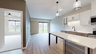 This well-appointed 2-bedroom, 1-bathroom residence at 6470 37th Ave NW in Rochester, MN offers a thoughtfully designed single-floor layout with modern finishes throughout. The open-concept kitchen and living area serves as the heart of the home, where light hardwood-style flooring, soft neutral tones, and a sliding glass door to the outdoors create a bright, welcoming atmosphere. The kitchen is a standout feature, boasting a large central island with a built-in beverage cooler, dual pendant lighting, stainless steel appliances, a subway tile backsplash, and a mix of white upper cabinetry and warm wood-toned lower cabinets. A frosted-glass interior door adds a refined architectural touch. The living area is open and spacious, benefiting from natural light streaming through the patio door. Both bedrooms feature plush carpeting, neutral warm-beige walls, and ample natural light from well-placed windows with outdoor views. The primary bedroom includes a closet for convenient storage. The full bathroom is clean and contemporary, featuring a tub-shower combo, wood-toned vanity with a white quartz countertop, and matching hardwood-style flooring. A dedicated entrance completes this well-organized and move-in-ready home.
