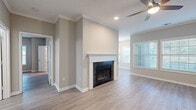 This single-floor residence offers a cohesive, modern aesthetic defined by light hardwood-style flooring, neutral gray and beige tones, and crisp white trim that flows consistently throughout every room. The spacious living area serves as the heart of the home, anchored by a striking dark-tiled fireplace with a white mantle surround and complemented by crown molding, recessed lighting, and a ceiling fan. Large windows with horizontal blinds invite generous natural light, creating a bright and airy atmosphere. An adjacent dining area features a glass-paneled exterior door flanked by wide windows, offering pleasant outdoor views and easy access to the outside. The galley-style kitchen is thoughtfully designed with gray shaker cabinets, white countertops, a subway tile backsplash, and a full suite of stainless steel appliances including a range, microwave, dishwasher, and refrigerator. The bedrooms are well-sized, each with ceiling fans, ample natural light, and the same warm hardwood-style flooring. The bathroom is finished with a dark gray shaker vanity, white countertop, framed mirror, and contemporary lighting. A welcoming entry hallway with crown molding and recessed lighting completes this clean, move-in ready home.
