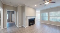 This single-floor residence offers a cohesive, modern aesthetic defined by light hardwood-style flooring, neutral gray and beige tones, and crisp white trim that flows consistently throughout every room. The spacious living area serves as the heart of the home, anchored by a striking dark-tiled fireplace with a white mantle surround and complemented by crown molding, recessed lighting, and a ceiling fan. Large windows with horizontal blinds invite generous natural light, creating a bright and airy atmosphere. An adjacent dining area features a glass-paneled exterior door flanked by wide windows, offering pleasant outdoor views and easy access to the outside. The galley-style kitchen is thoughtfully designed with gray shaker cabinets, white countertops, a subway tile backsplash, and a full suite of stainless steel appliances including a range, microwave, dishwasher, and refrigerator. The bedrooms are well-sized, each with ceiling fans, ample natural light, and the same warm hardwood-style flooring. The bathroom is finished with a dark gray shaker vanity, white countertop, framed mirror, and contemporary lighting. A welcoming entry hallway with crown molding and recessed lighting completes this clean, move-in ready home.
