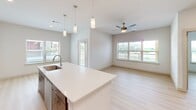 Located in Austin, TX, this well-designed 2-bedroom, 3-bathroom residence offers a thoughtful single-floor layout with modern finishes throughout. The kitchen is a standout feature, showcasing two-tone cabinetry with white upper cabinets and wood-grain lower cabinets, white quartz countertops, a subway tile backsplash, and stainless steel appliances including an electric range and built-in microwave. A kitchen island with pendant lighting connects seamlessly to the open living area, which is bathed in natural light from large windows and features a ceiling fan and direct access to a private balcony overlooking the surrounding community. Light wood-tone flooring flows consistently throughout the space, creating a clean and cohesive aesthetic. Both bedrooms are well-proportioned and bright, with large windows fitted with blinds. The spacious primary bedroom connects to an en-suite bathroom featuring a dual-sink vanity with wood-tone cabinetry, a large mirror, and a tub-shower combination with white tile surround. Two dedicated closets provide ample storage. The overall ambiance is clean, contemporary, and move-in ready, with a neutral color palette that lends itself well to personalization.