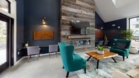Located at 1 Marys Way in Lincoln, Massachusetts, this single-floor community clubhouse combines modern design with thoughtful functionality. The space is defined by a striking deep navy blue color palette, soaring vaulted ceilings, and an abundance of natural light streaming through large, black-framed windows throughout.

The central gathering area serves as the heart of the space, anchored by a dramatic floor-to-ceiling reclaimed wood accent wall housing a sleek linear fireplace and mounted television. Polished concrete floors, rich wood furnishings, and vibrant teal accent chairs create a warm yet contemporary atmosphere. Large windows frame views of the surrounding neighborhood and greenery, enhancing the open, airy feel.

Adjacent to the lounge is a well-appointed kitchen featuring crisp white shaker cabinetry, dark granite countertops, a farmhouse-style stainless steel sink, and a classic white subway tile backsplash with matte black hardware throughout — a clean, stylish contrast to the bold navy walls.

The fitness center is generously sized and thoughtfully equipped, featuring rubber flooring, treadmills, a stationary bike, a dumbbell rack, an adjustable weight bench, and a dedicated stretching area. Tall windows flood the workout space with natural light and views of the outdoors, creating an energizing environment for exercise.
