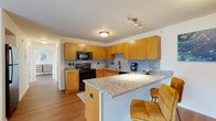 This single-floor residence presents a cohesive design language carried consistently across all rooms through warm wood tones, granite surfaces, and neutral walls. The kitchen serves as a central highlight, featuring rich honey-toned cabinetry extending to the ceiling for generous storage, complemented by granite countertops and a matching speckled tile backsplash. Black appliances, including a range, built-in microwave, dishwasher, and refrigerator, provide a clean contrast. A peninsula with granite overhang offers casual bar seating, connecting the kitchen to the living area and enhancing the open feel of the space. Hardwood flooring flows throughout, adding warmth underfoot.

The two bedrooms are well-proportioned, each receiving natural light from multiple windows with views of surrounding greenery. The primary bedroom features hardwood flooring and wall-mounted sconce lighting flanking the bed wall, while the second bedroom benefits from a bright, multi-window layout.

Both bathrooms maintain the design consistency of the home, each equipped with warm wood vanities, granite countertops, undermount sinks, large mirrors, and tile flooring. The overall ambiance is clean, modern, and functional, with a neutral palette that allows the natural materials to define the character of the space.