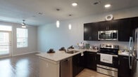 This single-floor residence offers a thoughtfully designed open-concept layout that seamlessly connects the kitchen and living areas. The kitchen is a standout feature, showcasing dark espresso cabinetry, granite-look countertops, and a full suite of stainless steel appliances including a refrigerator, electric range, microwave, and dishwasher. A peninsula with an integrated sink provides additional prep space and serves as a natural divide between the kitchen and the adjoining living area. Elegant pendant lighting hangs above the peninsula, complementing the recessed ceiling lights throughout. The living area features wood-look flooring, a ceiling fan, and a window that invites natural light into the space. The bedroom is carpeted for comfort, equipped with a ceiling fan, and offers access to a closet and an adjacent bathroom. The bathroom is finished with large-format wall tiles surrounding a soaking tub and shower combination, chrome fixtures, and wood-look flooring that ties back to the rest of the home. Neutral wall tones and clean white trim throughout the residence create a cohesive, contemporary ambiance that is both inviting and functional.