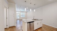 This thoughtfully laid-out one-bedroom, one-bathroom residence offers a cohesive and modern living experience across a single floor. The open-concept kitchen and living area serves as the heart of the home, anchored by a central island with granite countertops, an undermount stainless steel sink, and a built-in dishwasher. Three pendant lights hang above the island, adding a contemporary touch. The kitchen is fully equipped with stainless steel appliances, including a side-by-side refrigerator with ice and water dispenser, an electric range, over-the-range microwave, and white shaker-style cabinetry with a white subway tile backsplash. Warm hardwood-style flooring runs throughout the entire unit, complemented by crown molding and recessed lighting. The living area benefits from natural light streaming through multiple windows with blinds and direct access to an entry door. The bedroom is a comfortable retreat featuring a ceiling fan, two windows, and easy access to the well-appointed bathroom. The bathroom includes a dual-sink granite vanity with white cabinetry and leads directly into a spacious walk-in closet outfitted with built-in shelving and hanging rods, offering generous storage. The overall aesthetic is clean, bright, and modern.
