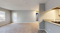 Located at 3555 Austell Rd in Marietta, Georgia, this single-floor residence offers a thoughtfully updated interior with a clean, neutral aesthetic throughout. The open living area is spacious and welcoming, featuring plush wall-to-wall carpeting, soft gray walls, and white trim that together create a bright, cohesive atmosphere. Multiple windows fitted with blinds allow generous natural light to fill the space, and a exterior-facing door provides convenient outdoor access.

The galley-style kitchen is a standout feature, finished with crisp white cabinetry, granite countertops, and a gray subway tile backsplash. Stainless steel appliances — including a gas range, dishwasher, and refrigerator — complement the light wood-look flooring, giving the kitchen a modern and functional character. A dedicated pantry or utility closet adds practical storage within the kitchen corridor.

The bathroom is finished in clean white tiling, featuring a full tub and shower combination with chrome fixtures. The textured ceilings are consistent throughout the unit, adding a classic residential touch. Overall, the space presents a well-maintained, move-in-ready interior with updated finishes in a convenient Marietta location.
