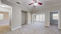 Located at 7585 Baymeadows Cir W in Jacksonville, Florida, this single-floor residence offers a well-designed layout with a clean, neutral aesthetic throughout. The main living area is generously proportioned, featuring plush wall-to-wall carpeting, elegant crown molding, and a ceiling fan with integrated lighting. Elevated ceilings lend an open, airy feel to the space, while a bank of windows floods the room with natural light and provides views of the surrounding greenery. A half-wall partition adds architectural interest and helps define the living space.

The kitchen is outfitted with white cabinetry, granite-style countertops, and black stainless steel appliances, including a refrigerator, range, and over-the-range microwave. Wood-look flooring runs throughout the kitchen, lending warmth and easy maintenance.

The bedroom is well-sized and carpeted, offering a walk-in closet with wire shelving systems that maximize storage. The bathroom is finished with a white vanity, granite countertop, framed mirror, a tub-shower combination with tiled surround, and wood-look flooring that ties back to the kitchen's aesthetic. The overall ambiance of the space is bright, tidy, and move-in ready.