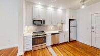 Located at N Ninth Street in Richmond, Virginia, this single-floor unit blends classic character with modern updates throughout. Rich, warm hardwood floors run continuously through the living spaces, adding a sense of history and warmth to the clean, contemporary aesthetic.

The kitchen is a standout feature, outfitted with crisp white shaker cabinetry extending to the ceiling for ample storage, light-toned countertops, a neutral tile backsplash, and a full suite of stainless steel appliances including a range, microwave, dishwasher, and refrigerator. Recessed lighting keeps the space bright and functional.

The open living area benefits from large, black-framed windows that invite abundant natural light and offer views of the surrounding urban streetscape. The white walls and recessed lighting create a clean, versatile canvas throughout.

The bedroom is generously proportioned, featuring the same hardwood floors and oversized windows with city views, providing both light and a connection to the neighborhood below.

A dedicated laundry area with a stacked washer and dryer unit adds everyday convenience, alongside built-in shelving for storage. The bathroom is finished with large-format floor tile, a tiled walk-in shower, granite vanity countertop, and brushed nickel fixtures, offering a polished and refined feel.
