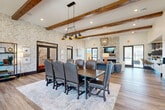 Located at 1220 Pleasant Ridge Rd in Greensboro, NC, this single-floor community clubhouse offers a thoughtfully designed gathering space blending rustic and contemporary elements. The den serves as the centerpiece, boasting exposed wood beam ceilings, designer geometric wallcovering, and rich hardwood-style flooring. A floor-to-ceiling stacked stone fireplace anchors the room, complemented by an elegant chandelier and a large conference-style dining table with upholstered leather chairs — ideal for both social gatherings and meetings. The kitchen features deep navy shaker cabinetry, subway tile backsplash, stone countertops, and stainless steel appliances, providing a fully functional space for entertaining. Two covered patios extend the living space outdoors. The first patio is a spacious lounge area with vaulted ceilings, multiple ceiling fans, and a stone fireplace surrounded by comfortable seating. The second patio opens to views of the community grounds, including a playground, picnic areas, and a large resort-style pool with pergolas and lounge seating. The overall ambiance is welcoming and upscale, with abundant natural light and seamless indoor-outdoor connectivity throughout.