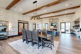 Located at 1220 Pleasant Ridge Rd in Greensboro, NC, this single-floor community clubhouse offers a thoughtfully designed gathering space blending rustic and contemporary elements. The den serves as the centerpiece, boasting exposed wood beam ceilings, designer geometric wallcovering, and rich hardwood-style flooring. A floor-to-ceiling stacked stone fireplace anchors the room, complemented by an elegant chandelier and a large conference-style dining table with upholstered leather chairs — ideal for both social gatherings and meetings. The kitchen features deep navy shaker cabinetry, subway tile backsplash, stone countertops, and stainless steel appliances, providing a fully functional space for entertaining. Two covered patios extend the living space outdoors. The first patio is a spacious lounge area with vaulted ceilings, multiple ceiling fans, and a stone fireplace surrounded by comfortable seating. The second patio opens to views of the community grounds, including a playground, picnic areas, and a large resort-style pool with pergolas and lounge seating. The overall ambiance is welcoming and upscale, with abundant natural light and seamless indoor-outdoor connectivity throughout.