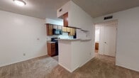 Located at 8301 N Council Rd in Oklahoma City, Oklahoma, this single-floor unit offers a practical and comfortable layout designed for everyday living. The kitchen is configured as a galley-style space, featuring warm wood-toned cabinetry, granite-look countertops, and black appliances including an electric range, built-in microwave, and refrigerator. Wood-look flooring runs through the kitchen, adding a clean, durable surface for high-traffic use. A peninsula breakfast bar connects the kitchen to the adjoining living area, creating an open, functional flow between the two spaces. The living room is generously proportioned, finished with plush wall-to-wall carpeting, and features a ceiling fan with a light fixture. A set of patio-style French doors allows natural light to fill the room while providing outdoor access. The bedroom is a well-sized, carpeted room equipped with its own ceiling fan and a window fitted with blinds for natural light and privacy. A closet is accessible directly from the bedroom. Throughout the unit, textured ceilings, neutral wall tones, and consistent finishes create a cohesive, understated aesthetic. HVAC vents are present in key areas, ensuring climate control throughout the space.