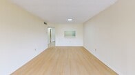 Located in Miami, FL, this one-bedroom, one-bathroom apartment offers a well-organized layout across a single floor. The living room is a bright, open space featuring light wood laminate flooring, soft cream-toned walls, and a textured ceiling. A large sliding glass door floods the room with natural light and opens directly onto a private balcony, where mature trees and lush greenery create a tranquil outdoor setting. A pass-through window connects the living area to the adjacent kitchen space, adding a functional architectural detail. The bedroom is generously sized, also finished with light wood flooring, and includes two closet options: a spacious walk-in closet with full wire shelving systems, and an additional reach-in closet with built-in shelves — providing exceptional storage. The bathroom features tile flooring, a wide vanity with an oversized mirror, and a full tub-shower combination with warm-toned tile surround and decorative mosaic accents. A hallway connects the rooms efficiently, and an entrance area welcomes residents into the space. Throughout the unit, neutral tones, consistent flooring, and ample natural light contribute to a clean, functional, and comfortable living environment.