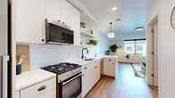 This single-floor residence offers a thoughtfully designed layout that balances modern aesthetics with everyday functionality. The kitchen is a standout feature, outfitted with crisp white cabinetry, open floating shelves, and a classic subway tile backsplash. Stainless steel appliances — including a gas range, built-in microwave, refrigerator, and dishwasher — are complemented by sleek black hardware and a matte black sink faucet, creating a clean, contemporary contrast. Warm hardwood flooring runs continuously throughout the space, lending a cohesive and inviting feel. The living area is bathed in natural light from a large picture window that frames views of the surrounding urban streetscape, creating an airy, open atmosphere. A wall-mounted mini-split unit ensures comfortable climate control year-round. The bathroom maintains the home's clean design sensibility, featuring a tiled shower, hardwood floors, and a calm, neutral palette. Throughout the unit, thoughtful touches such as recessed lighting, pendant fixtures, and abundant greenery contribute to a warm, lived-in character. The open-plan configuration maximizes the sense of space, making this residence a well-rounded and functional urban dwelling.