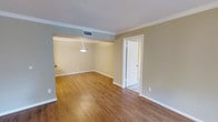 This single-floor space offers a clean, functional layout with thoughtful architectural details throughout. The interior is finished with warm-toned hardwood flooring that flows seamlessly across the open living and dining areas, adding both warmth and visual continuity to the space. Crown molding lines the ceilings, lending a classic, polished character to the rooms.

The living area transitions naturally into a defined dining space, which is subtly delineated by a soffit overhead and illuminated by a pendant light fixture that serves as a tasteful focal point. The neutral, earthy wall tones complement the light-colored ceilings and white trim, creating a bright and inviting ambiance throughout.

A doorway off the main living area provides access to an additional room, offering flexible use of the space. The interior benefits from a central HVAC system with ceiling vents ensuring consistent climate control. White baseboards and door casings throughout reinforce a crisp, cohesive aesthetic.

Overall, this space presents a straightforward and well-appointed layout suitable for a variety of uses, combining classic finishing touches with practical design in a single-level configuration.