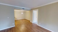 This single-floor space offers a clean, functional layout with thoughtful architectural details throughout. The interior is finished with warm-toned hardwood flooring that flows seamlessly across the open living and dining areas, adding both warmth and visual continuity to the space. Crown molding lines the ceilings, lending a classic, polished character to the rooms.

The living area transitions naturally into a defined dining space, which is subtly delineated by a soffit overhead and illuminated by a pendant light fixture that serves as a tasteful focal point. The neutral, earthy wall tones complement the light-colored ceilings and white trim, creating a bright and inviting ambiance throughout.

A doorway off the main living area provides access to an additional room, offering flexible use of the space. The interior benefits from a central HVAC system with ceiling vents ensuring consistent climate control. White baseboards and door casings throughout reinforce a crisp, cohesive aesthetic.

Overall, this space presents a straightforward and well-appointed layout suitable for a variety of uses, combining classic finishing touches with practical design in a single-level configuration.