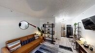 This single-floor unit at 14255 Northwest Fwy in Houston, Texas, offers a thoughtfully arranged layout that maximizes its compact footprint. The living area serves as the central gathering space, featuring light wood-tone laminate flooring, crisp white walls, and a textured ceiling throughout. A front-facing window allows natural light to filter into the room, complementing the wall-mounted HVAC unit positioned beneath it. The living space is anchored by a warm caramel leather sofa accented with patterned throw pillows, a bold geometric area rug, and decorative touches including a round wall mirror and an open metal-and-wood shelving unit that provides both storage and visual interest.

Transitioning toward the back of the unit, the kitchen is a compact yet functional space outfitted with light wood cabinetry, dark countertops, a stainless steel sink, and full-size appliances including a refrigerator and microwave. A modern sputnik-style chandelier adds a contemporary design accent overhead.

The bathroom features a tub-shower combination finished with striking marble-patterned wall surrounds in white and grey, paired with brushed nickel fixtures that lend a clean, polished look. Overall, the unit presents a cohesive, modern aesthetic that balances practicality with contemporary style.