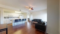 This single-floor residence offers a well-organized layout that connects the main living areas seamlessly. The living room is a comfortable, open space finished with rich dark hardwood flooring and served by a ceiling fan overhead. Large windows dressed with horizontal blinds allow generous natural light to filter in while providing views of surrounding greenery. Black leather seating and a central coffee table complete the area.

The kitchen is efficiently designed with white cabinetry extending to the ceiling, a mosaic tile backsplash, and white appliances including a range, built-in microwave, and refrigerator. A peninsula counter with bar seating integrates the kitchen with the living and dining areas, and a stainless steel sink adds functionality.

The bedrooms are carpeted and well-proportioned, each featuring windows with natural light. One bedroom includes a built-in desk, wall-mounted shelving, and a walk-in closet, making it particularly functional. Ceiling fans are present in select bedrooms.

Two bathrooms serve the unit, each finished with light tile flooring and white vanities. One bathroom features a tub-shower combination with full tile surround, while the other includes a vanity with under-sink storage and a window for natural ventilation.