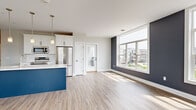 Located at 300 YMCA Way in Penfield, NY, this well-designed 2-bedroom, 1-bathroom residence offers a thoughtfully planned single-floor layout with contemporary finishes throughout. The open-concept kitchen and living area serves as the heart of the home, centered around a striking navy blue island with a white quartz countertop and pendant lighting overhead. White shaker-style cabinetry, stainless steel appliances — including a French door refrigerator, range, and built-in microwave — and light wood-tone flooring complete the kitchen's modern aesthetic. A door off the kitchen provides convenient access to an outdoor area. The living room is defined by large, oversized windows along a bold dark accent wall, flooding the space with natural light and offering views of the surrounding community and greenery. A bright, well-lit hallway with clean white panel doors connects the main living area to the private rooms. Both bedrooms feature light wood-tone flooring, neutral walls, and generously sized windows with outdoor views. The primary bedroom is comfortably sized, providing a peaceful retreat. The bathroom is finished with a white shaker vanity, quartz countertop, large mirror, and black hardware accents, maintaining a clean and modern design consistent with the rest of the home.