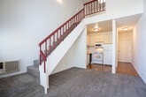 Located in Walnut Creek, CA, this two-story, 1-bedroom, 1-bathroom home offers a well-planned layout spread across two floors. The main level features hardwood flooring throughout the entry hallway, kitchen, and bathroom, while plush carpet defines the open-concept living and dining area. The kitchen is outfitted with white cabinetry, a full suite of white appliances including a refrigerator, range, and microwave, and connects seamlessly to the living space beneath a striking open staircase with a bold red railing — a standout architectural detail that adds character to the interior. Soaring vaulted ceilings rise dramatically over the living area, enhancing the sense of openness. A wall of tall windows at the front of the home floods the space with natural light and frames peaceful views of surrounding trees. The upper level, accessed via the staircase, houses the carpeted bedroom, which benefits from a skylight overhead and a baseboard heater, along with a dedicated closet. The full bathroom features warm hardwood-style flooring, a combined tub and shower, and a vanity with ample counter space. A hallway connects the main living areas efficiently, completing this thoughtfully designed two-level home.