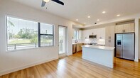 Located at 2480 First St in Fort Myers, FL, this well-appointed single-story home offers three bedrooms, two bathrooms, and a thoughtfully designed floor plan. The open-concept kitchen and living area serves as the heart of the home, featuring light wood-tone and white cabinetry, quartz countertops, stainless steel appliances including a French door refrigerator, built-in microwave, and range, as well as a central island ideal for casual dining or meal prep. Large windows flood the space with natural light and offer views of the surrounding greenery, while a ceiling fan enhances comfort. Warm-toned hardwood-style flooring flows consistently throughout the home, complementing the clean white walls and modern black hardware accents. The hallway connects the bedrooms efficiently, each room featuring windows with outdoor views of the lush Florida landscape and ceiling fans for year-round comfort. The generously sized primary bedroom includes ample closet space, and the home boasts six closets in total for exceptional storage. A dedicated laundry room houses a full-size washer and dryer. The included patio provides an outdoor retreat. The overall aesthetic is clean, contemporary, and move-in ready.