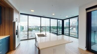 Located in the heart of Atlanta's Midtown neighborhood, this contemporary residence at 1150 Spring St NW offers a refined urban living experience defined by clean lines, modern finishes, and abundant natural light. The open-plan living and kitchen area serves as the centerpiece of the space, anchored by a large island with a white quartz countertop and an undermount sink with a sleek gooseneck faucet. The kitchen is outfitted with navy blue cabinetry complemented by warm walnut wood accents, a reflective ceramic tile backsplash, and stainless steel appliances including a French door refrigerator, range, and over-the-range microwave. Expansive floor-to-ceiling windows with black frames wrap the living area, framing sweeping views of the Atlanta skyline and cityscape while filling the space with natural light. Light-toned hardwood flooring flows throughout the main living areas, creating a warm, cohesive aesthetic. The bedroom features plush carpeting, a ceiling fan, and large windows offering additional city views. The bathroom presents a dual-sink vanity with navy cabinetry, white countertops, and a large mirror. A second bathroom off the hallway mirrors this design with a double vanity and ample storage. Together, the thoughtful design elements and prime Midtown location make this a distinctly contemporary urban retreat.