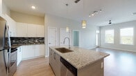 This well-appointed single-floor residence offers a thoughtfully designed open-concept layout that seamlessly connects the kitchen, dining, and living areas. The kitchen serves as the centerpiece of the space, anchored by a large granite-topped island with an undermount sink, pendant lighting, and an integrated dishwasher. Crisp white cabinetry extends to the ceiling, complemented by a striking black-and-white mosaic tile backsplash and a full suite of stainless steel appliances, including a range, over-the-range microwave, and refrigerator. Light wood-look flooring flows throughout the main living areas, enhancing the bright and airy atmosphere created by multiple windows and a ceiling fan in the living room. The primary bedroom features direct access to a private en-suite bathroom with a granite vanity, glass-enclosed walk-in shower, and a spacious walk-in closet. A secondary bedroom offers plush carpeting and generous natural light through dual windows with outdoor views. The second bathroom is finished with a full soaking tub, tiled surround, and a matching granite vanity. Throughout the space, neutral tones and clean lines create a cohesive, modern aesthetic that is both functional and inviting.