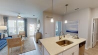 This single-floor residence offers a thoughtfully designed open layout with modern finishes throughout. The kitchen serves as a central hub, featuring white shaker cabinetry with brushed nickel hardware, quartz countertops, stainless steel appliances including a French door refrigerator, range, microwave, and dishwasher. A peninsula island with an undermount sink and pendant lighting provides both additional prep space and casual seating.

The living room benefits from natural light through large windows with exterior views, complemented by a ceiling fan and direct access to a private patio. Adjacent to the living area, a dedicated dining space accommodates a full dining set and features a decorative mirror.

Two bedrooms offer comfortable retreats; one with carpeted floors and large windows bringing in natural light, and the primary bedroom finished in neutral tones. The bathroom is outfitted with a glass-enclosed shower, quartz vanity, white cabinetry, and wood-look flooring. A dedicated in-unit laundry area with full-size washer and dryer and built-in shelving adds practical convenience. Light wood-look flooring flows consistently throughout the main living areas, contributing to the home's cohesive, contemporary aesthetic.