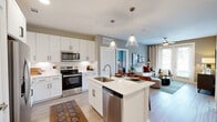 Located at 4103 Rogers Rd in San Antonio, TX, this well-appointed 1-bedroom, 2-bathroom single-story home offers a thoughtfully designed layout with modern finishes throughout. The open-concept kitchen is a standout feature, showcasing crisp white shaker cabinetry, quartz countertops, a herringbone tile backsplash, stainless steel appliances, and a central island with a double sink illuminated by stylish pendant lighting. The kitchen flows seamlessly into the living room, which is anchored by a ceiling fan, light wood-style flooring, and French doors that open to a private patio with views of lush green landscaping. The spacious primary bedroom features a ceiling fan, soft accent wall tones, and direct access to a full ensuite bathroom complete with a dual-sink vanity, white cabinetry, and a tiled tub-shower combination. A versatile office with large windows, ample natural light, and a ceiling fan provides an ideal workspace or flex room. Additional highlights include a dedicated laundry area with a full-size washer and dryer, four closets for generous storage, a second full bathroom, and a hallway connecting the well-organized floor plan. The community exterior features manicured grounds and contemporary architecture.