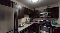 Located on Biljana Drive in Louisville, Kentucky, this single-floor space offers a thoughtfully designed layout with multiple functional areas. The kitchen is a standout feature, outfitted with rich dark espresso cabinetry, granite countertops, and a full suite of stainless steel appliances including a range, over-the-range microwave, dishwasher, and refrigerator. Dark hardwood-style flooring flows through much of the space, adding warmth and visual continuity.

The dining area accommodates a glass-top table beneath a contemporary drum pendant light, with an accent wall in a warm golden tone complemented by framed artwork. French doors in one of the office spaces flood the room with natural light and provide outdoor access, creating an airy, professional atmosphere. A second carpeted office features a ceiling fan with light and a window overlooking greenery, offering a quieter workspace.

The bathroom includes durable hardwood-style flooring, a shower-tub combination with a decorative curtain, and additional closet storage. A dedicated laundry area houses a stacked washer and dryer unit, adding everyday convenience. Throughout, neutral wall tones, textured ceilings, and carefully chosen décor contribute to a cohesive, functional ambiance.