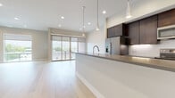 This single-floor residence showcases a thoughtfully designed open-concept layout with a seamless flow between the kitchen and living areas. The kitchen is a standout feature, outfitted with rich dark-espresso cabinetry extending to the ceiling, stainless steel appliances including a refrigerator with ice dispenser, an electric range, and built-in microwave. A classic white subway tile backsplash adds a clean contrast, while a large waterfall-edge island with a gray countertop and sleek pendant lighting serves as the centerpiece of the space. Light hardwood flooring runs throughout the main living areas, contributing to a bright, airy ambiance. The living area is generously proportioned, bathed in natural light through large sliding glass doors that open to an outdoor space, complemented by a modern ceiling fan and recessed lighting. The primary bathroom features dual vanities with teal-blue cabinetry, gray tile flooring, a walk-in glass shower with white subway tile, and a separate soaking tub. A secondary bathroom offers a tub-shower combo with matching subway tile and dark vanity cabinetry. A spacious walk-in closet with built-in shelving and hanging rods provides excellent storage. Neutral wall tones and clean white trim complete the polished, contemporary aesthetic throughout.