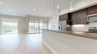 This single-floor residence showcases a thoughtfully designed open-concept layout with a seamless flow between the kitchen and living areas. The kitchen is a standout feature, outfitted with rich dark-espresso cabinetry extending to the ceiling, stainless steel appliances including a refrigerator with ice dispenser, an electric range, and built-in microwave. A classic white subway tile backsplash adds a clean contrast, while a large waterfall-edge island with a gray countertop and sleek pendant lighting serves as the centerpiece of the space. Light hardwood flooring runs throughout the main living areas, contributing to a bright, airy ambiance. The living area is generously proportioned, bathed in natural light through large sliding glass doors that open to an outdoor space, complemented by a modern ceiling fan and recessed lighting. The primary bathroom features dual vanities with teal-blue cabinetry, gray tile flooring, a walk-in glass shower with white subway tile, and a separate soaking tub. A secondary bathroom offers a tub-shower combo with matching subway tile and dark vanity cabinetry. A spacious walk-in closet with built-in shelving and hanging rods provides excellent storage. Neutral wall tones and clean white trim complete the polished, contemporary aesthetic throughout.