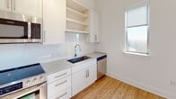 Located at 650 E Brooklyn Village Ave in Charlotte, NC, this single-floor unit offers a clean, modern aesthetic throughout. The open layout is anchored by warm hardwood-style flooring that flows seamlessly across the main living areas, complemented by crisp white walls and recessed lighting that create a bright, welcoming atmosphere. Large windows invite generous natural light into the living space, where a generous footprint provides flexible arrangement options.

The kitchen is a standout feature, outfitted with white shaker-style cabinetry, grey countertops, a tile backsplash, and a full suite of stainless steel appliances including a refrigerator with ice maker, gas range, built-in microwave, and dishwasher. A deep undermount sink sits beneath a window, adding both functionality and natural light to the workspace. Track lighting above ensures ample illumination for cooking and entertaining.

A secondary room features light vinyl flooring, high clerestory windows, and pendant lighting, making it well-suited for use as an office or flex space. The walk-in closet is equipped with multi-tiered wire shelving systems for organized storage and features plush carpeting underfoot. Throughout the unit, clean lines and a neutral color palette establish a contemporary and functional living environment.