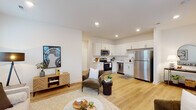 This well-designed two-floor home offers a bright, contemporary interior highlighted by light hardwood flooring and crisp white walls throughout. The main level opens into a welcoming living area bathed in natural light from multiple windows, seamlessly connecting to a fully equipped kitchen. The kitchen features white shaker-style cabinetry, white quartz countertops, and a full suite of stainless steel appliances including a range, over-the-range microwave, dishwasher, and refrigerator. A convenient half bathroom is also located on the main floor. A staircase leads to the upper level, where the primary bedroom offers a generous layout with direct access to a private en-suite bathroom. The en-suite is finished with a white vanity, quartz countertop, and a glass-enclosed shower. An additional bedroom on this floor provides a bright, versatile space with a window overlooking the exterior. A dedicated laundry area with a full-size washer and dryer completes the upper level. Recessed lighting, clean architectural lines, and a cohesive neutral palette give the home a polished, modern ambiance throughout.