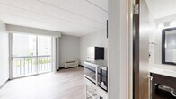 Unit 329 at 1722 N Walnut St is a efficiently designed studio located in Bloomington, Indiana. The single-floor layout makes smart use of its compact footprint, combining the living and kitchen areas into one open, functional space.

The main living area features light-toned luxury vinyl plank flooring throughout, neutral gray walls, and a tiled drop ceiling that lends a clean, uniform look. A wall-mounted television bracket and a wall sconce add practical touches to the space. A sliding glass door fills the room with natural light and opens to a private balcony with outdoor views, creating a bright and airy atmosphere. A wall-unit HVAC system ensures year-round climate control.

The kitchenette is positioned along one wall and includes dark espresso cabinetry, a full-size refrigerator, a microwave, a sink with a white countertop, and a compact utility cart for additional workspace. The layout keeps all essentials accessible within a tight, organized footprint.

A short hallway connects the main living area to the bathroom, which continues the light vinyl plank flooring. The bathroom features a dark-framed vanity mirror, a white countertop sink set into espresso cabinetry, and a shower/tub combination. Bright vanity lighting above the mirror ensures a well-lit grooming space. The overall design is clean, modern, and functional throughout.