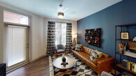 This thoughtfully designed single-floor residence showcases a cohesive color palette of navy blue, warm wood tones, and crisp white surfaces throughout. The open-concept kitchen is a standout feature, outfitted with rich navy shaker-style cabinetry, stainless steel appliances including a refrigerator, range, and microwave, and a generous white quartz island with an undermount sink and pendant lighting overhead. Wood-look flooring ties the kitchen seamlessly into the living and dining areas.

The living room offers a relaxed yet curated ambiance, highlighted by a bold blue accent wall, hardwood-style flooring, and a ceiling fan, with natural light filtering in through large windows dressed in patterned drapes.

Two well-sized bedrooms each feature their own distinctive accent wall — one in deep burgundy and another in forest green — along with plush carpeting, ceiling fans, and natural light. Each bedroom connects to a spacious walk-in closet outfitted with built-in dark wood shelving systems, hanging rods, and integrated drawers for ample organization.

The bathrooms are finished with navy vanity cabinetry, white quartz countertops, and wood-look flooring. One bathroom includes a tub-shower combination with subway tile surround and built-in open shelving, while the other serves as a private en-suite off the primary bedroom.