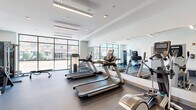 Located in Memphis, TN, this modern fitness center offers a well-appointed single-floor exercise room designed for a comprehensive workout experience. The space features a clean, contemporary aesthetic with white walls, recessed and linear LED lighting, and durable rubber flooring throughout, creating a professional and functional atmosphere.

Large, floor-to-ceiling grid-pane windows line the walls, flooding the interior with abundant natural light while providing open views of the surrounding Memphis streetscape. Full-length mirrors on one wall visually expand the space and support proper form during exercise.

The cardio zone is equipped with multiple treadmills and an elliptical trainer, while the strength training area features a multi-functional cable machine, a Precor weight station, an adjustable weight bench, and a rack of dumbbells in varying weights. This diverse equipment selection supports both cardiovascular and resistance training needs.

A glass-partitioned entry with double doors connects the fitness center to an adjacent space, accented with bold yellow details that add a vibrant touch. A hand sanitizer dispenser is conveniently positioned near the entrance. The overall design balances functionality with modern style, making this fitness center a practical and inviting facility for users in Memphis, TN.