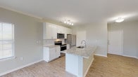 This single-floor residence at 100 S Kirkwood Rd in Kirkwood, Missouri offers a thoughtfully designed open-concept layout with a bright, contemporary aesthetic. The kitchen is a standout feature, equipped with crisp white shaker cabinetry, granite countertops, a herringbone tile backsplash, and a full suite of stainless steel appliances including a range, microwave, and refrigerator. A central island with an undermount sink and additional granite counter space provides both functionality and a natural gathering point that flows seamlessly into the living and dining areas. Crown molding and an elegant chandelier add refined touches to the dining space, while large windows bathe the open living area in natural light and offer pleasant outdoor views. Light-toned hardwood flooring runs throughout the main living spaces, lending a clean and cohesive feel. The bedroom features plush carpeting, a ceiling fan, and dual windows that invite ample daylight and treetop views. The bathroom is finished with a granite-topped vanity, white cabinetry, and brushed nickel hardware, including a grab bar for added accessibility. The overall ambiance is fresh, modern, and move-in ready.
